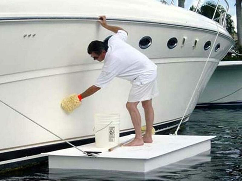 Man stands on floating EPS expanded polystyrene Styrofoam platform cleaning a boat